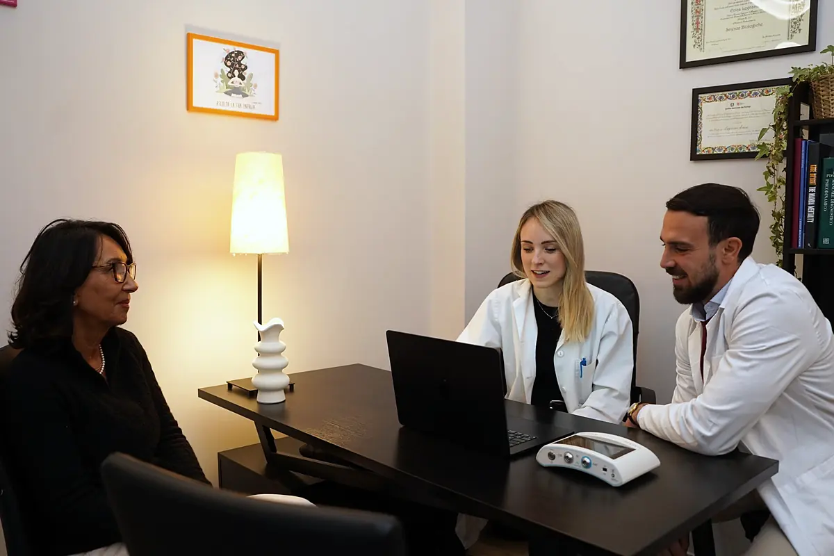 Due professionisti di discipline diverse, seduti alla stessa scrivania, parlano insieme con una persona.